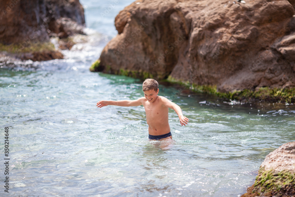 Fototapeta premium Happy beautiful teenager is swimming in the sea, a boy comes out of the water