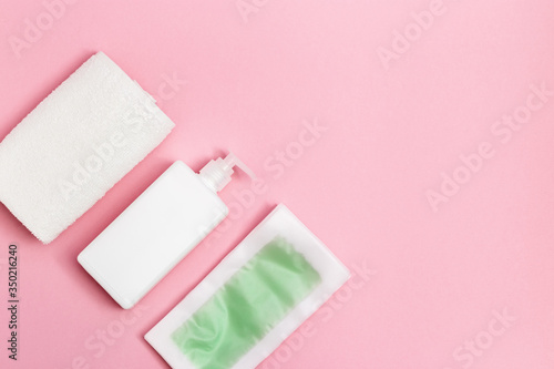 Set of disposable wax strips for depilation, body moisturizer and white cotton towel on pink background with copy space. Hair removal procedure. Top view.