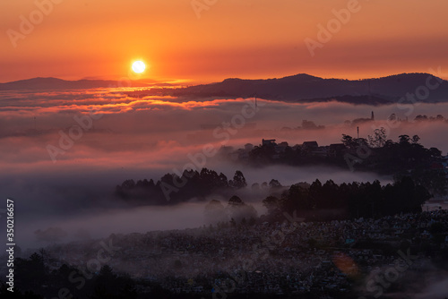 Fototapeta Naklejka Na Ścianę i Meble -  Mountains in fog at beautiful morning in autumn in Dalat city, Vietnam. Landscape with Langbiang mountain valley, low clouds, forest, colorful sky , city illumination at dusk.