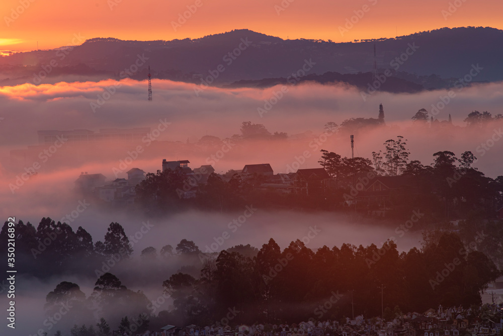 Obraz premium Mountains in fog at beautiful morning in autumn in Dalat city, Vietnam. Landscape with Langbiang mountain valley, low clouds, forest, colorful sky , city illumination at dusk.