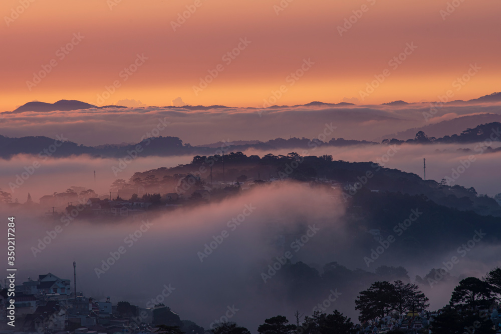 Obraz premium Mountains in fog at beautiful morning in autumn in Dalat city, Vietnam. Landscape with Langbiang mountain valley, low clouds, forest, colorful sky , city illumination at dusk.