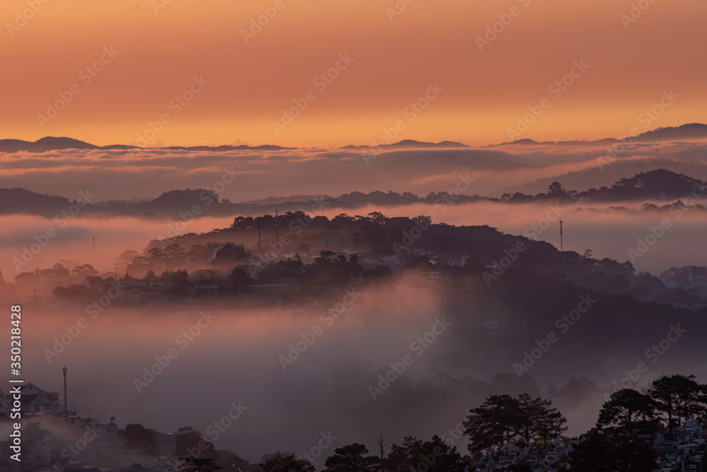 Obraz premium Mountains in fog at beautiful morning in autumn in Dalat city, Vietnam. Landscape with Langbiang mountain valley, low clouds, forest, colorful sky , city illumination at dusk.