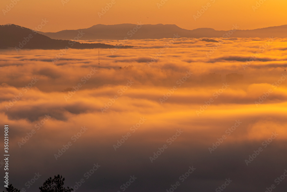 Obraz premium Mountains in fog at beautiful morning in autumn in Dalat city, Vietnam. Landscape with Langbiang mountain valley, low clouds, forest, colorful sky , city illumination at dusk.