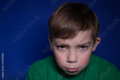portrait of a sad pensive nine year old blond boy on a blue background