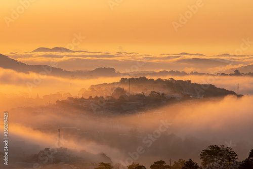 Mountains in fog at beautiful morning in autumn in Dalat city, Vietnam. Landscape with Langbiang mountain valley, low clouds, forest, colorful sky , city illumination at dusk.