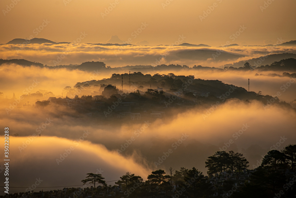 Obraz premium Mountains in fog at beautiful morning in autumn in Dalat city, Vietnam. Landscape with Langbiang mountain valley, low clouds, forest, colorful sky , city illumination at dusk.