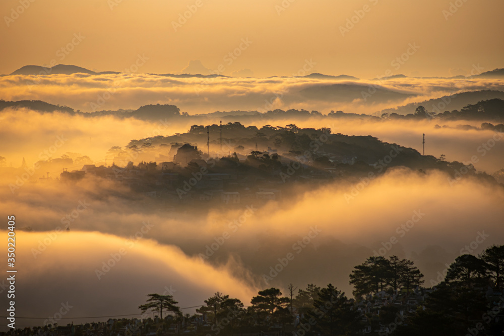 Mountains in fog at beautiful morning in autumn in Dalat city, Vietnam. Landscape with Langbiang mountain valley, low clouds, forest, colorful sky , city illumination at dusk. Mountains in fog at beautiful morning in autumn in Dalat city, Vietnam. Landscape with Langbiang mountain valley, low clouds, forest, colorful sky , city illumination at dusk.