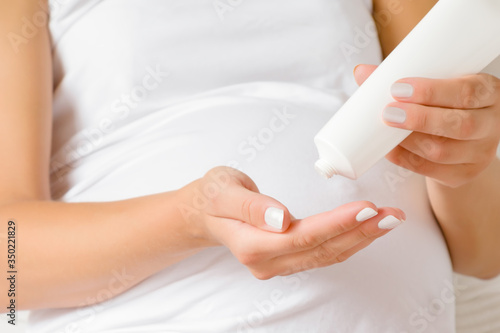 Young woman hand holding white tube and using moisturizing cream. Care about perfect, soft and smooth skin in pregnancy time. Closeup. Front view.
