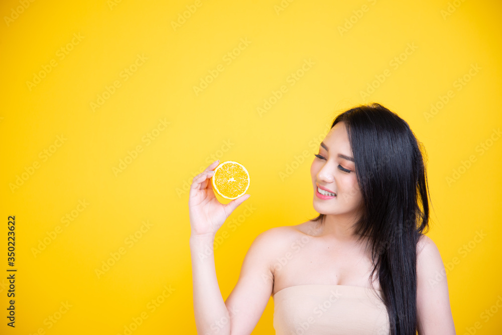 Beautiful Asian women smile happyness holding fresh orange slide with a yellow background.Squeeze Fresh oranges healthy fruits that are vitamin C. Beautiful Asian women smile happyness holding fresh orange slide with a yellow background.Squeeze Fresh oranges healthy fruits that are vitamin C.