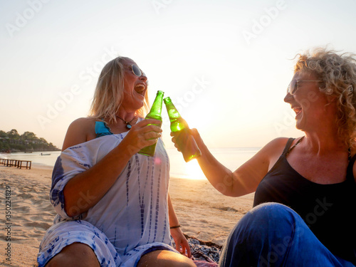 Two senior women laughing and having beer at sea shore at sunny day