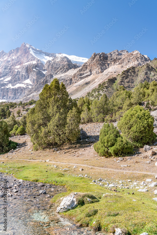 The beautiful mountain trekking road with clear blue sky and rocky hills and fresh mountain stream in Fann mountains in Tajikistan The beautiful mountain trekking road with clear blue sky and rocky hills and fresh mountain stream in Fann mountains in Tajikistan