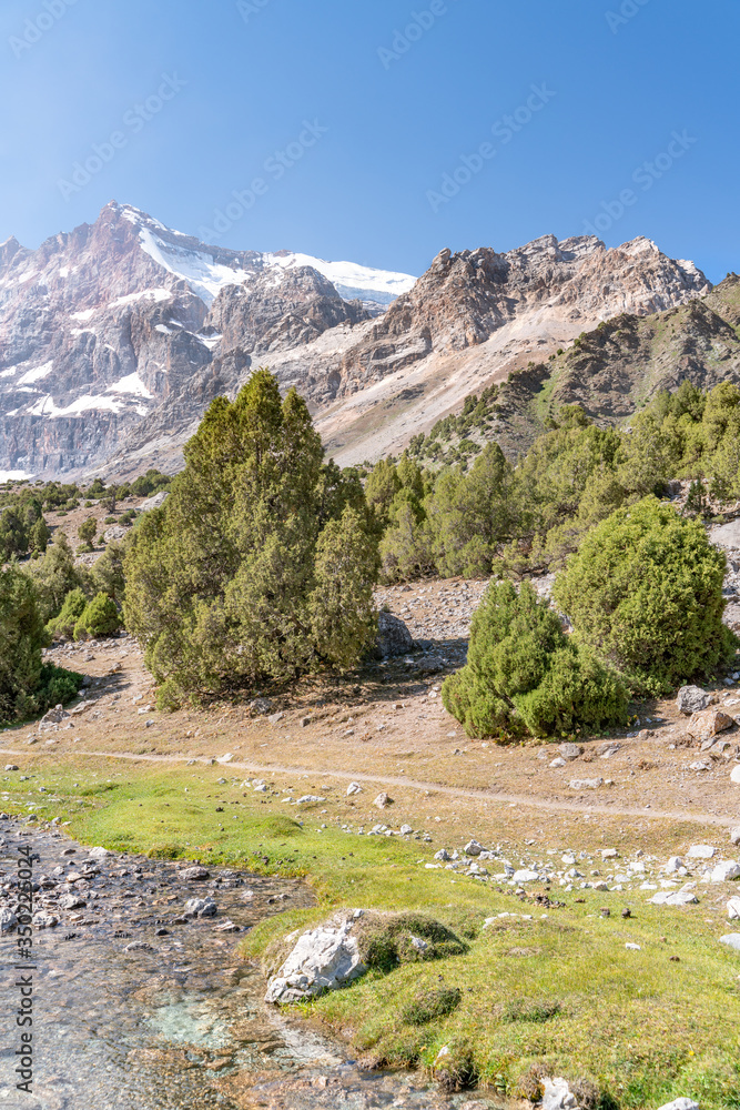 The beautiful mountain trekking road with clear blue sky and rocky hills and fresh mountain stream in Fann mountains in Tajikistan