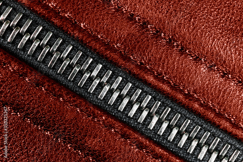 Macro shot of zipper on red leather texture background with stitching. Horizontal background from a close-up of red leather material