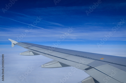 View over the clouds from the porthole of an airplane with plane wing and blue sky