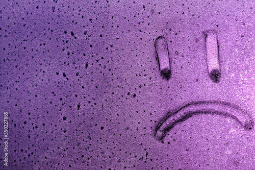 Smiley sad face drawing on glass in purple light with water drops and copy space