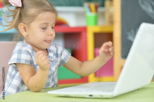 Portrait of curious little girl using laptop at desk
