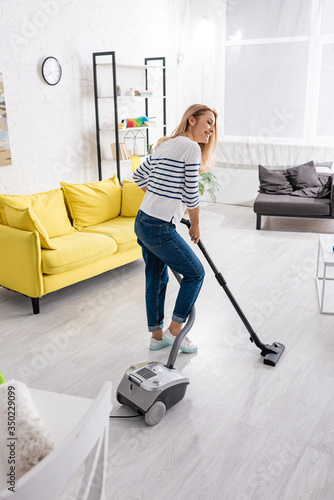 Attractive woman smiling and cleaning up with vacuum cleaner in living room