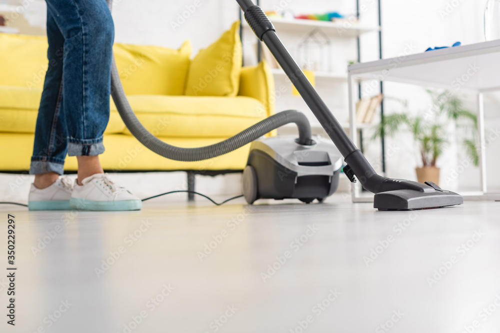 Fototapeta premium Cropped view of woman with vacuum cleaner near coffee table in living room