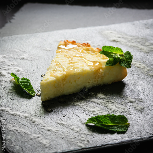 cheesecake sprinkled with icing sugar and with sweet syrup with mint leaves on a black pond