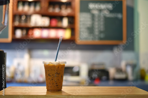 Iced coffee in plastic glass on wooden background in coffee shop. Selected focus