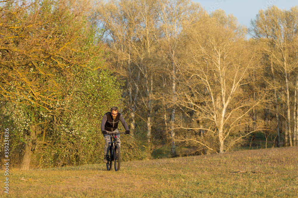 Sports brutal bearded guy on a modern mountain bike. Cyclist on the green hills in the spring.