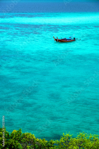 Fototapeta Naklejka Na Ścianę i Meble -  The sea looks out to emerald blue. There is 1 floating boat quietly on the waves in the Andaman Sea. At Sunset Beach, Koh Lipe, Satun, Southern Thailand