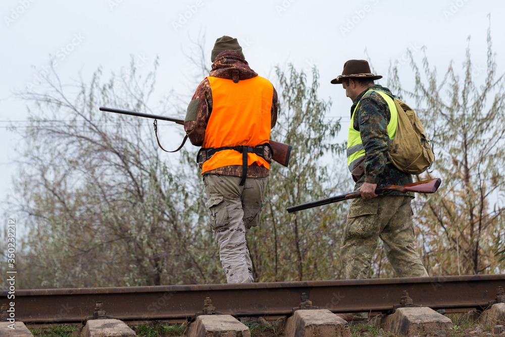 A mans with a gun in his hands and an orange vest on a pheasant hunt in a wooded area in cloudy weather. Hunters with dogs in search of game. A mans with a gun in his hands and an orange vest on a pheasant hunt in a wooded area in cloudy weather. Hunters with dogs in search of game.