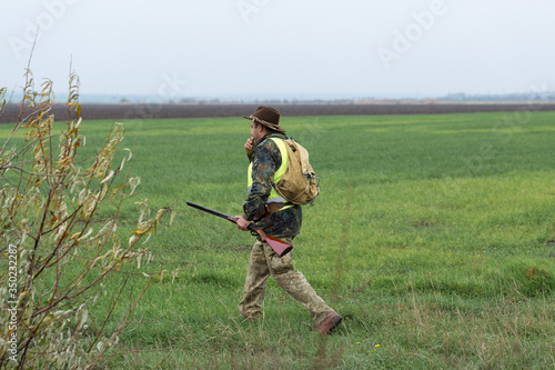 Hunting period, autumn season open. A hunter with a gun in his hands in hunting clothes in the autumn forest in search of a trophy. A man stands with weapons and hunting dogs tracking down the game.