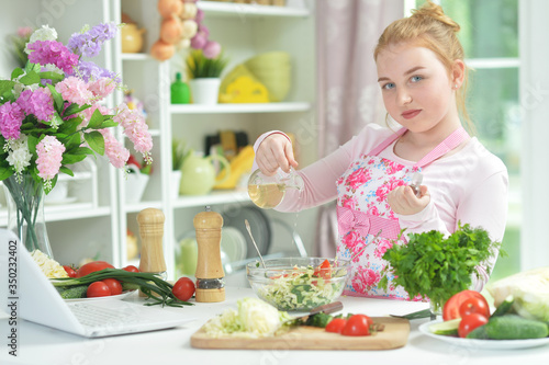 Cute teen girl preparing fresh salad on kitchen table