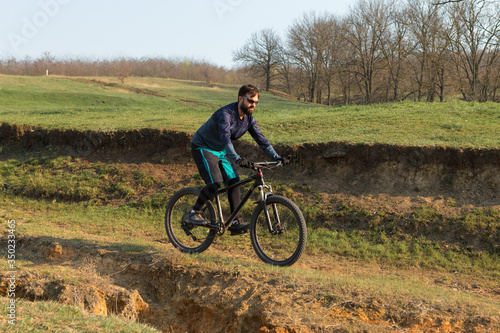 Cyclist in shorts and jersey on a modern carbon hardtail bike with an air suspension fork standing on a cliff against the background of fresh green spring forest