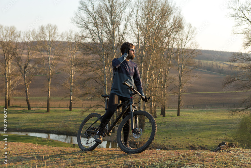 Obraz premium Cyclist in shorts and jersey on a modern carbon hardtail bike with an air suspension fork standing on a cliff against the background of fresh green spring forest