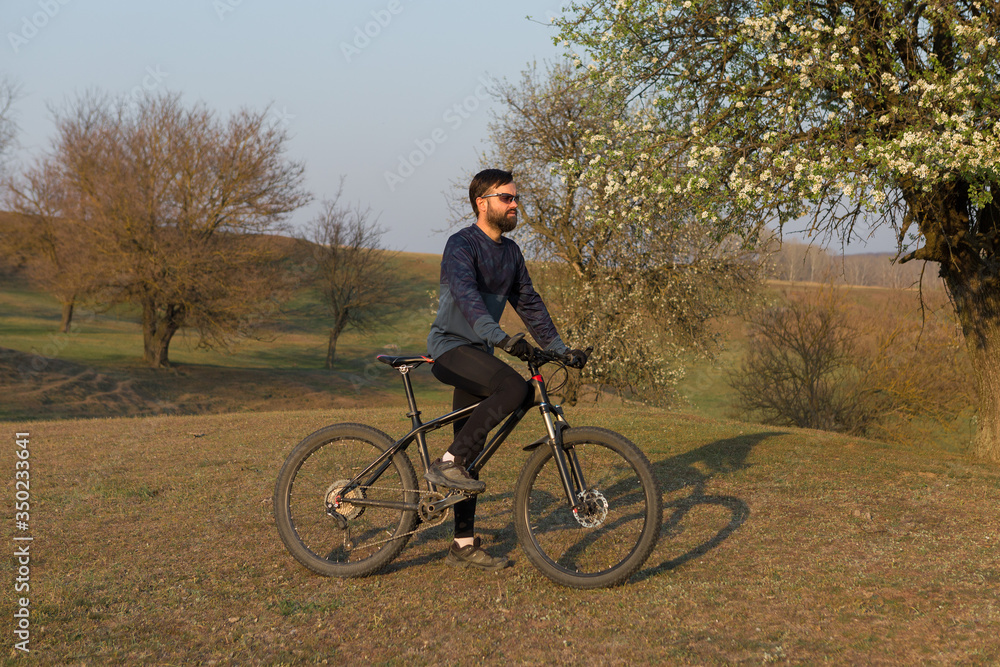 Cyclist in shorts and jersey on a modern carbon hardtail bike with an air suspension fork standing on a cliff against the background of fresh green spring forest