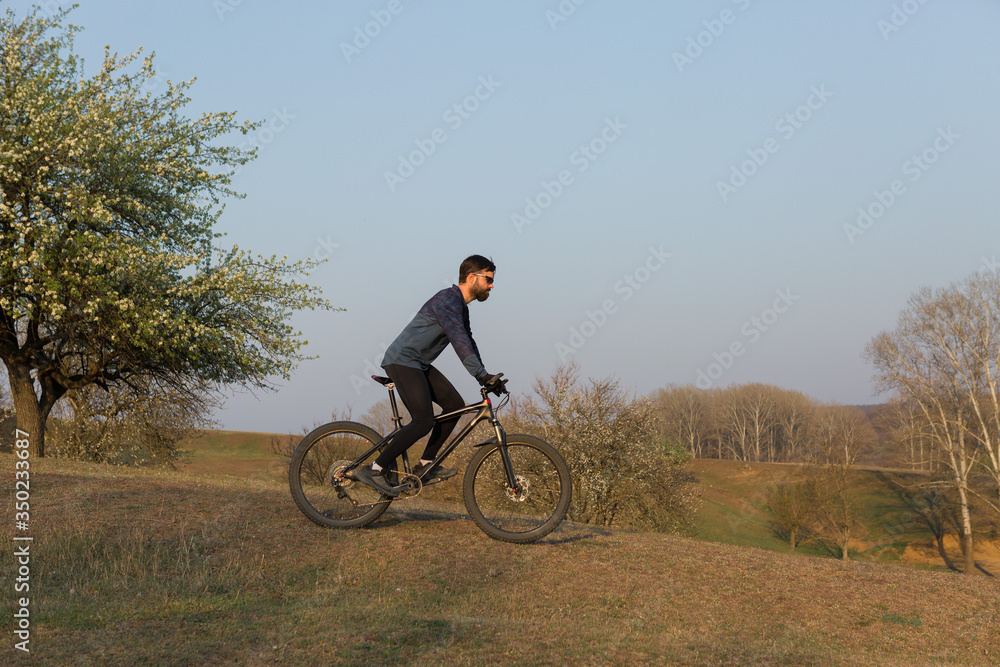 Cyclist in shorts and jersey on a modern carbon hardtail bike with an air suspension fork standing on a cliff against the background of fresh green spring forest