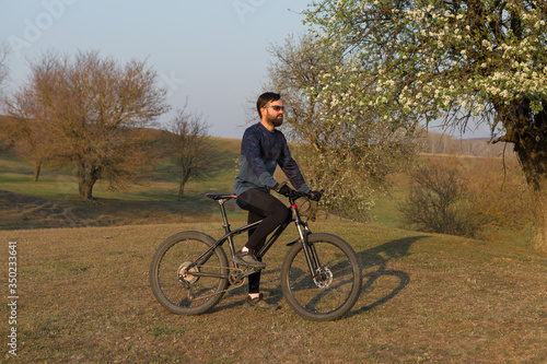 Fototapeta Naklejka Na Ścianę i Meble -  Cyclist in shorts and jersey on a modern carbon hardtail bike with an air suspension fork standing on a cliff against the background of fresh green spring forest