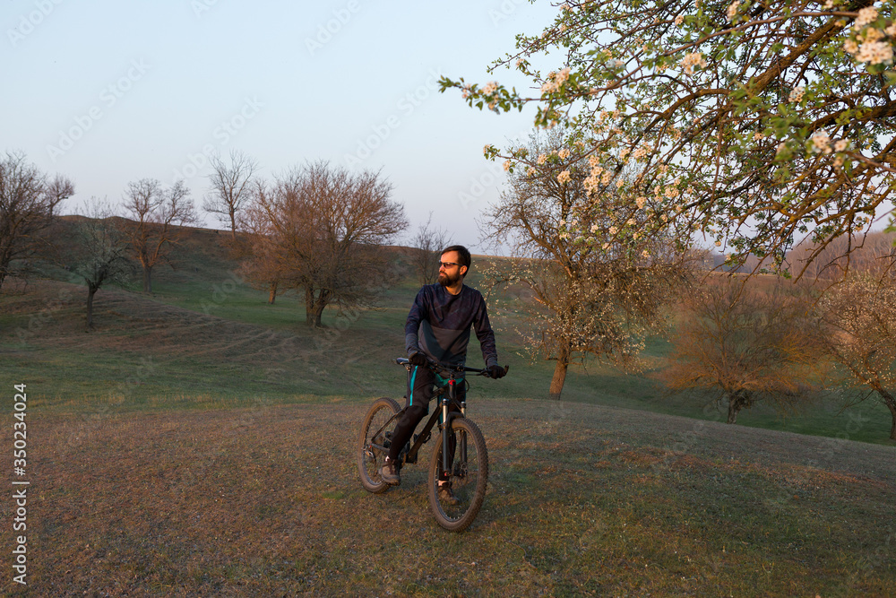 Cyclist in shorts and jersey on a modern carbon hardtail bike with an air suspension fork standing on a cliff against the background of fresh green spring forest