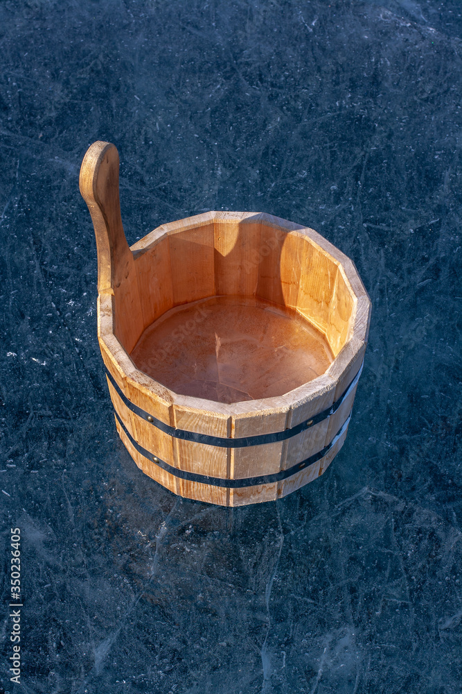 A wooden tub with ice inside is on ice. Ice with bubbles and cracks. Iron tightening rings connect parts of the tub. Sunny. Vertical. A wooden tub with ice inside is on ice. Ice with bubbles and cracks. Iron tightening rings connect parts of the tub. Sunny. Vertical.