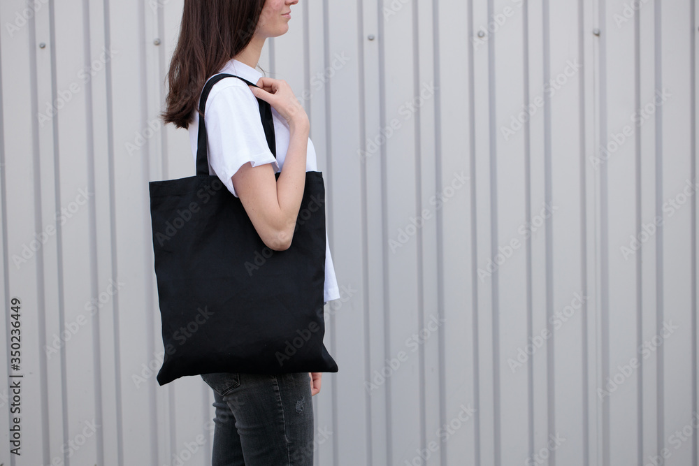 Young woman holding black textile eco bag against white wall. Ecology or environment protection concept. Black eco bag for mock up. Young woman holding black textile eco bag against white wall. Ecology or environment protection concept. Black eco bag for mock up.