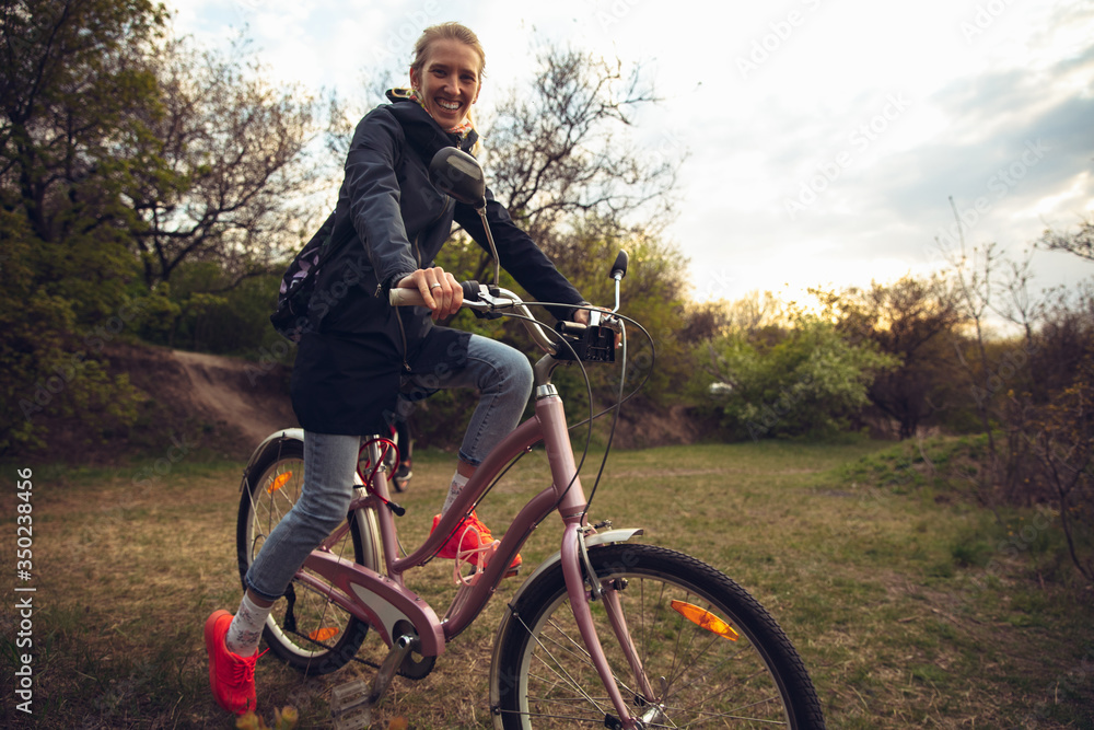 Obraz premium Young woman having fun near countryside park, riding bike, traveling at spring day. Calm nature, spring day, positive emotions. Sportive, active leisure activity. Walking in motion, blossoming nature.