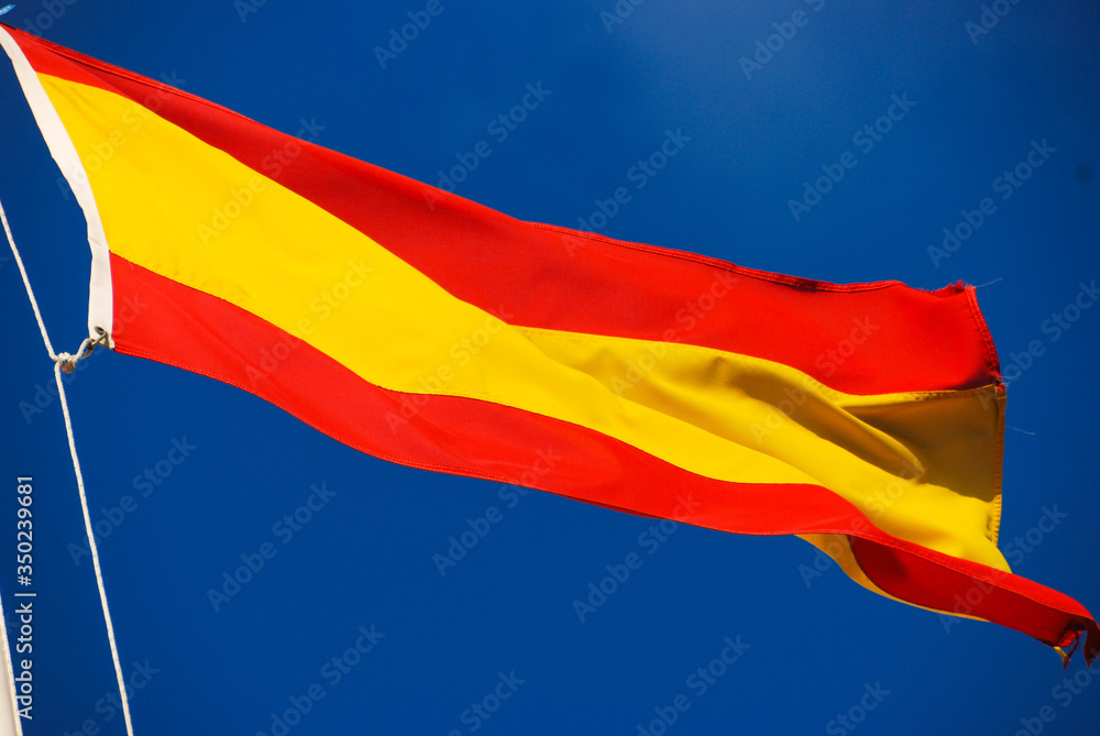 flag of the kingdom of spain waving in the wind over blue sky in the background flag of the kingdom of spain waving in the wind over blue sky in the background