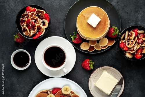 The concept of a delicious breakfast. Coffee and mini pancakes with strawberries, bananas, nuts in a plate and American pancakes in a plate on a stone background 