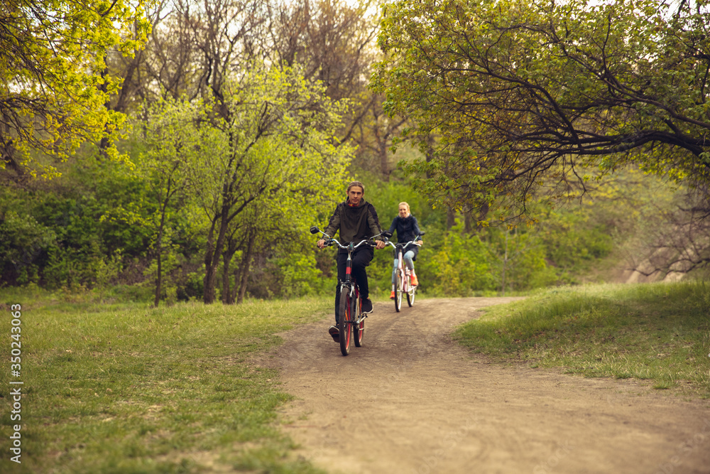 Fototapeta premium Best friends having fun near countryside park, riding bikes, spending time healthy. Calm nature, spring day, positive emotions. Sportive, active leisure activity. Traveling or walking together.