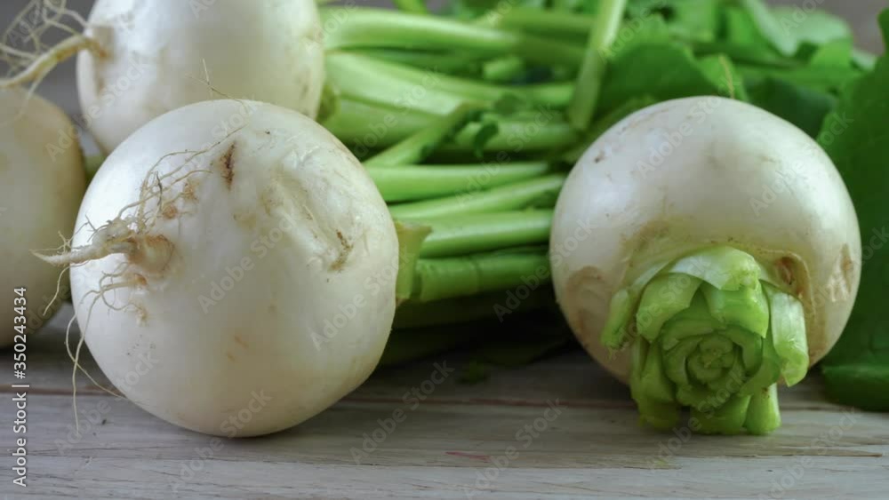 Bunch of white turnips on wooden background. Close up view of fresh spring vegetable with green leaves. 4k video, panning shot Bunch of white turnips on wooden background. Close up view of fresh spring vegetable with green leaves. 4k video, panning shot