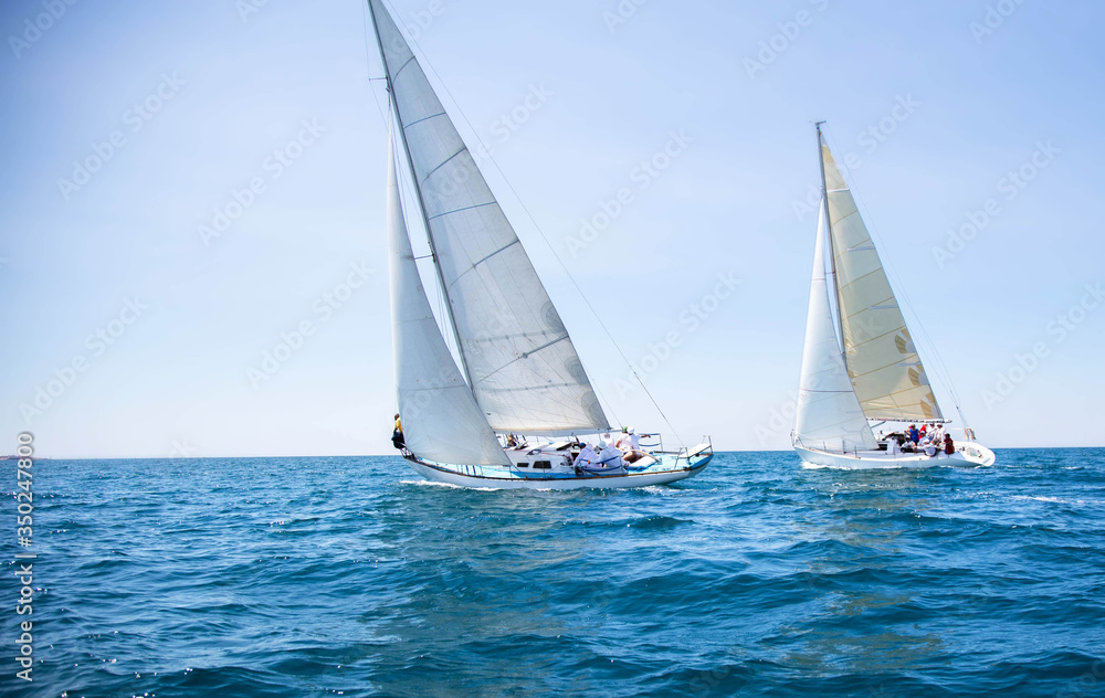 Two white motor yachts with raised sails take part in the regatta. A strong wind tipped the ship. Waves, a small wave amplify emotions at competitions. Boat crews are busy navigating and chasing. Boat