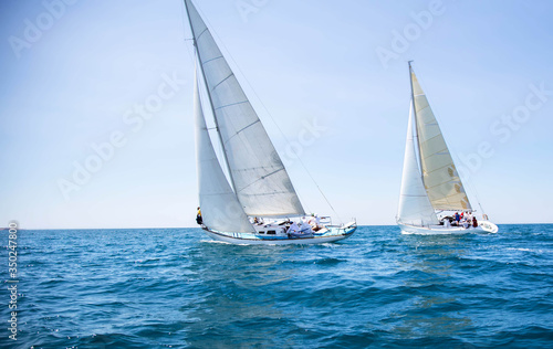 Two white motor yachts with raised sails take part in the regatta. A strong wind tipped the ship. Waves, a small wave amplify emotions at competitions. Boat crews are busy navigating and chasing. Boat