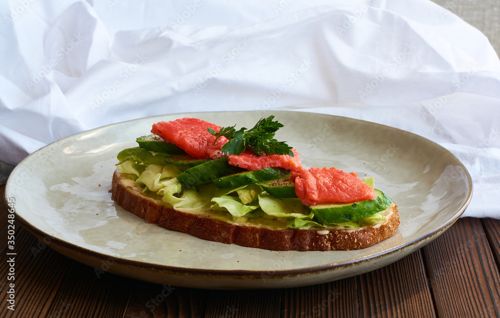 Large toast of rye bread with cheese, cabbage, parsley, fresh cucumber and red fish salmon on wooden background with white cloth drapery. Large toast of rye bread with cheese, cabbage, parsley, fresh cucumber and red fish salmon on wooden background with white cloth drapery.