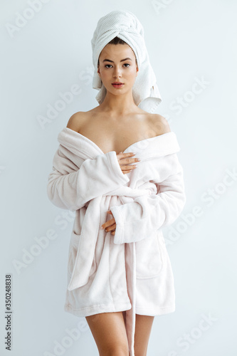 Beautiful young woman wrapped in white bath towel preparing for sauna, studio background