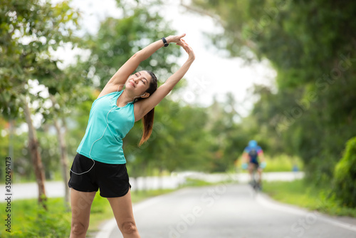 Healthy woman warming up before jogging run and relax stretching her arms and looking away in the road outdoor. Asian runner people workout fitness session  nature park background. Healthy Lifestyle 