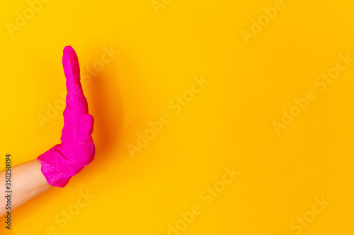 Hand in pink protective rubber glove greeting, waving isolated on yellow studio background with copyspace. Gesturing, holding, presenting things. Negative space for your advertising. Showing, pointing