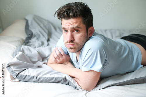 Young man laying in bed, looks worried and unsatisfied