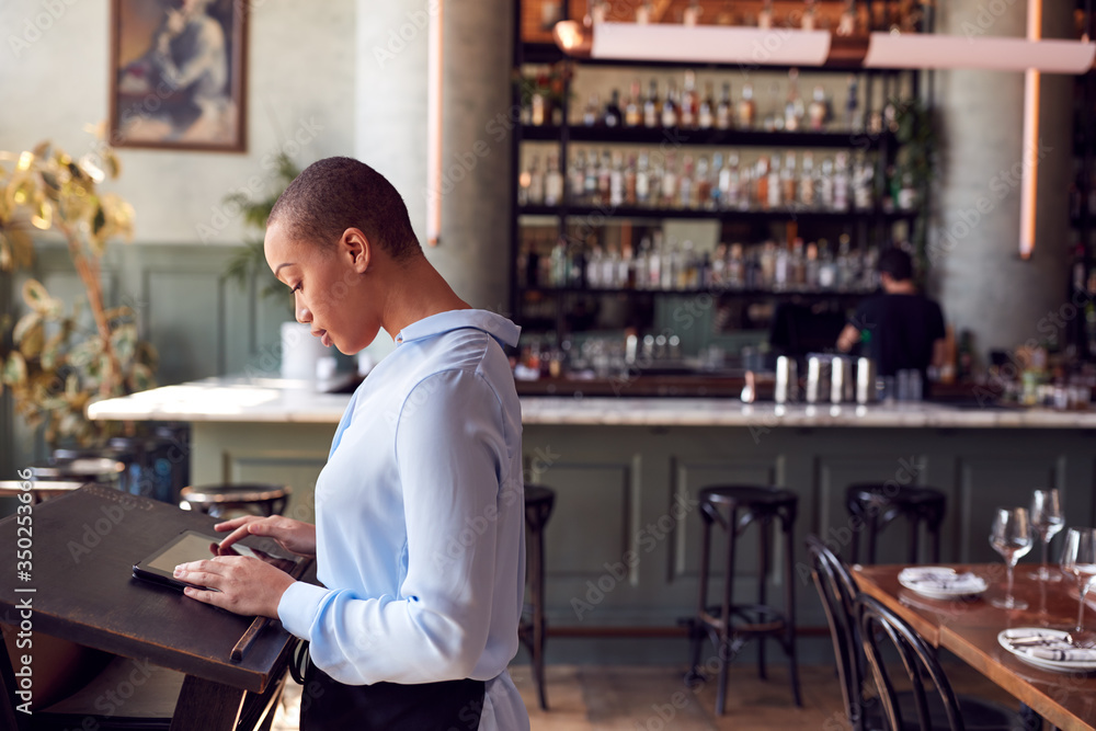 Female Owner Of Restaurant Bar Standing At Counter Using Digital Tablet Female Owner Of Restaurant Bar Standing At Counter Using Digital Tablet